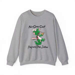 Puede incluir: Una sudadera gris con un dragón verde de dibujos animados que lleva un gorro de cocinero y sostiene una rebanada de pizza. El texto "No One Out Papas The John" está impreso en la sudadera.