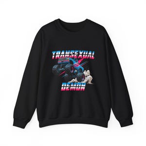 May include: Black sweatshirt featuring a graphic of a blue monster truck with pink and blue accents, kicking up dust. The text "TRANSSEXUAL DEMON" is displayed above and below the truck in pink and blue.