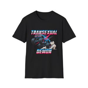 May include: Black t-shirt featuring a graphic of a monster truck with the text "TRANSSEXUAL DEMON" in pink and blue. The monster truck is blue and red, kicking up dust. The design is centered on the shirt.