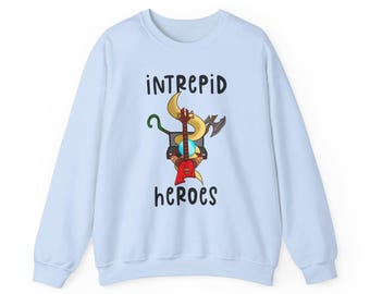 May include: Light blue sweatshirt with the words "INTREPID heroes" in black. The graphic features a cartoon design with a guitar, axe, and other elements. The sweatshirt is made of a soft material and has long sleeves.