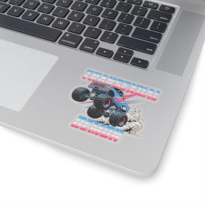 May include: A sticker featuring a blue monster truck with large black tires, kicking up dust. The text "TRANSSEXUAL DEMON" is displayed in a blue and pink gradient across the top and bottom of the sticker.