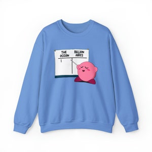 Peut inclure: Un sweat-shirt bleu clair avec un personnage de dessin animé rose tenant un pointeur et pointant vers le mot "Billion Aires" sur un tableau blanc. Le tableau blanc comporte également les mots "The Ocean" écrits dessus.
