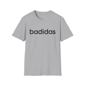 Può includere: T-shirt grigio chiaro con la scritta "badidas" in nero sul petto. La maglietta ha un girocollo e maniche corte. Il testo è in un font sans-serif. Il tessuto sembra leggero.