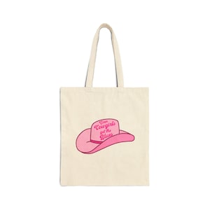 Può includere: Una borsa tote rosa con un cappello da cowboy rosa e la scritta "Even Cowgirls get the Blues" stampata su di essa.