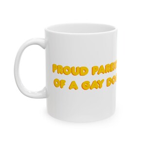 Peut inclure: Mug en céramique blanche avec l'inscription "PROUD PARENTS OF A GAY DOG" en lettres jaunes à bulles. La tasse a une anse incurvée et une finition brillante. Le texte est centré sur la tasse.