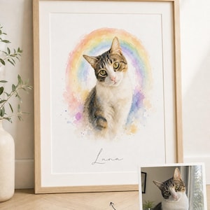 May include: A framed watercolor-style portrait of a tabby and white cat named Luna, positioned in front of a soft-colored rainbow. The artwork is displayed in a light wood frame, accompanied by a small reference photograph of the same cat.