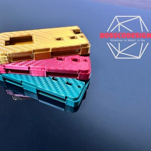 Pode incluir: Três capas de telefone impressas em 3D empilhadas umas sobre as outras. A capa superior é dourada, a capa do meio é rosa e a capa inferior é turquesa. As capas têm um padrão de fibra de carbono.