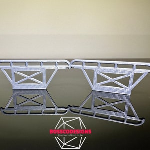 May include: Two silver 3D printed metal truck bed racks. The racks are designed with a grid pattern and have a curved top.