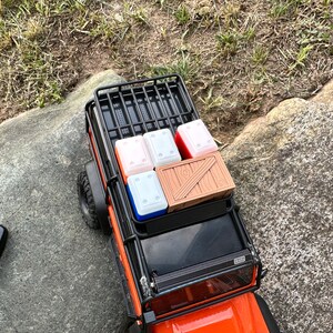 Peut inclure: Un porte-bagages de toit en m&eacute;tal noir avec une caisse en bois et quatre conteneurs rouges et blancs sur le toit d'un camion jouet orange.
