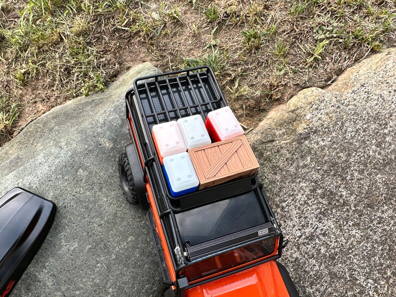 Peut inclure: Un porte-bagages de toit en m&eacute;tal noir avec une caisse en bois et quatre conteneurs rouges et blancs sur le toit d'un camion jouet orange.