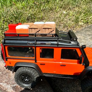 Peut inclure: Camion jouet orange avec un porte-bagages de toit noir et une caisse en bois sur le dessus. Le camion a des roues noires et un pare-chocs noir.