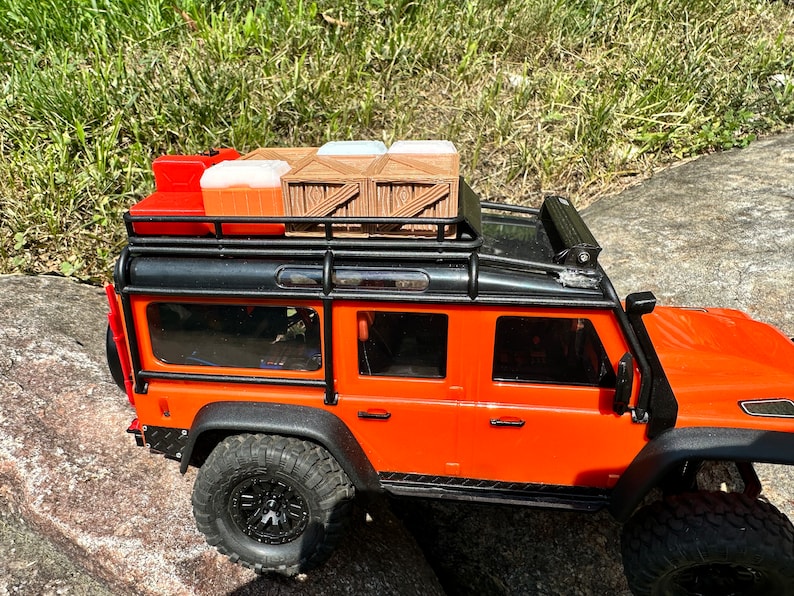 Peut inclure: Camion jouet orange avec un porte-bagages de toit noir et une caisse en bois sur le dessus. Le camion a des roues noires et un pare-chocs noir.
