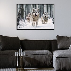 May include: A framed print featuring a pack of wolves running through a snowy forest. The wolves have gray and white fur, and the forest has tall, slender trees. The artwork is displayed on a white wall above a dark gray sofa.