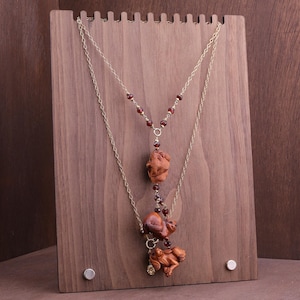 May include: Two-strand necklace with carved wooden monkey pendants and red bead accents. The necklaces are displayed on a wooden jewelry stand. The monkey pendants are brown and detailed.