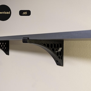 May include: Black metal shelf brackets with a honeycomb design. The brackets are attached to a dark gray shelf.
