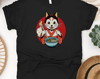 May include: Black t-shirt featuring a cartoon cat wearing a kimono and holding chopsticks over a bowl of noodles. The cat is set against a red circle, with a small flame on the left. The cat has a white face, black ears, and is smiling.