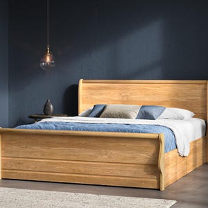 May include: A wooden bed with a headboard and footboard. The bed is made of light-coloured wood and has a sleigh bed design. The bed is made up with white sheets, blue blankets, and pillows. The room has a dark blue wall.
