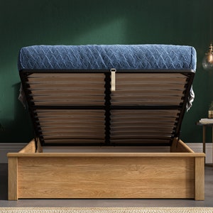 May include: A wooden bed frame with a blue quilted mattress. The bed frame has a lift-up mechanism to reveal storage space underneath.