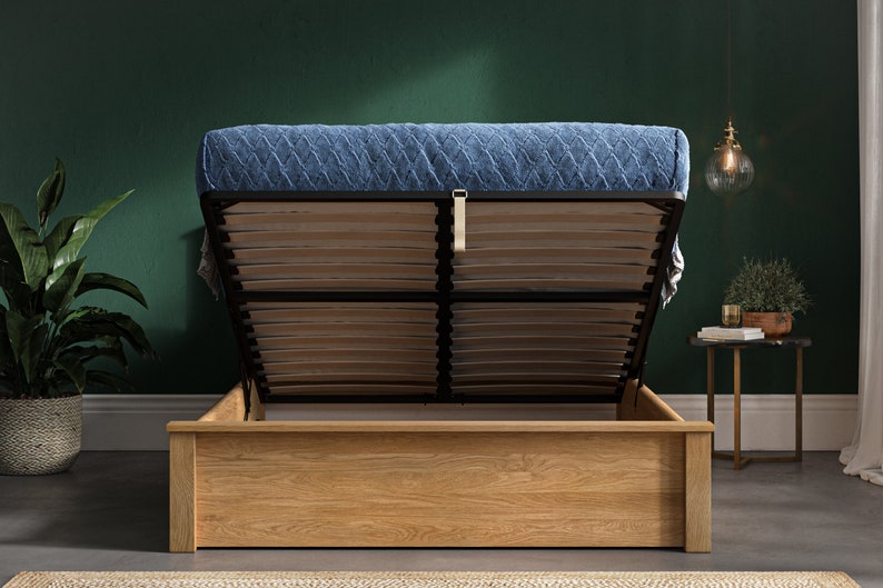 May include: A wooden bed frame with a blue quilted mattress. The bed frame has a lift-up mechanism to reveal storage space underneath.