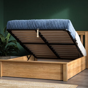 May include: A wooden bed frame with a lift-up storage compartment. The bed frame is made of light brown wood and has a black metal frame. The mattress is blue and has a quilted pattern.