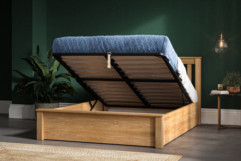 May include: A wooden bed frame with a lift-up storage compartment. The bed frame is made of light brown wood and has a black metal frame. The mattress is blue and has a quilted pattern.