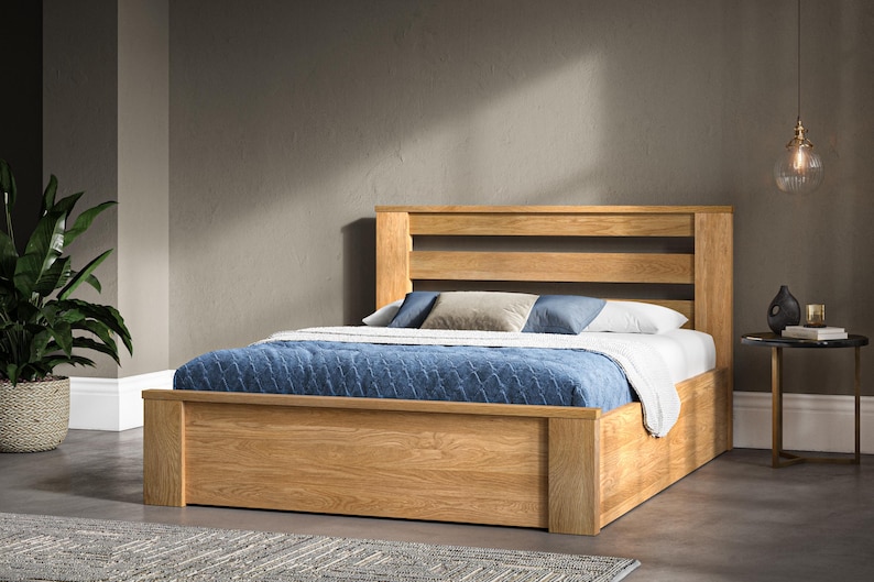 May include: A wooden bed frame with a slatted headboard and a storage drawer underneath. The bed is made with a blue and white patterned bedspread and pillows.