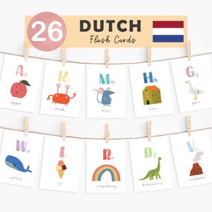 Op de afbeelding: Een set van 26 Nederlandse flashcards, elk met een letter en een illustratie. De kaarten zijn met houten knijpers aan een touwtje bevestigd. De banner bovenaan leest "DUTCH Flash Cards" met de Nederlandse vlag.