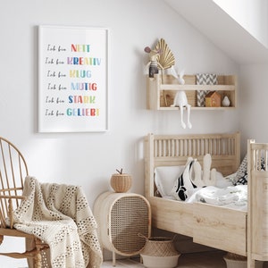 May include: A white framed print with colourful text in German that reads "Ich bin" followed by a list of positive adjectives: nett, kreativ, klug, mutig, stark, geliebt. The print is hanging on a white wall in a child's bedroom.