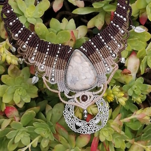 May include: A brown and beige macrame necklace with a silver pendant and a large, white agate stone. The necklace is decorated with small silver beads and has a delicate, intricate design.