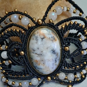 May include: A black macrame bracelet with a white and brown agate gemstone and gold beads.