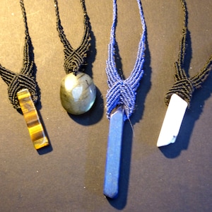 May include: Four necklaces with different gemstone pendants. The necklaces are made with black and blue cord and feature a tiger's eye, labradorite, lapis lazuli, and white quartz pendant.
