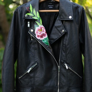 Puede incluir: Chaqueta de cuero negra para moto con un dise&ntilde;o floral pintado en el cuello. El dise&ntilde;o presenta una flor rosa, hojas verdes y bayas rojas.