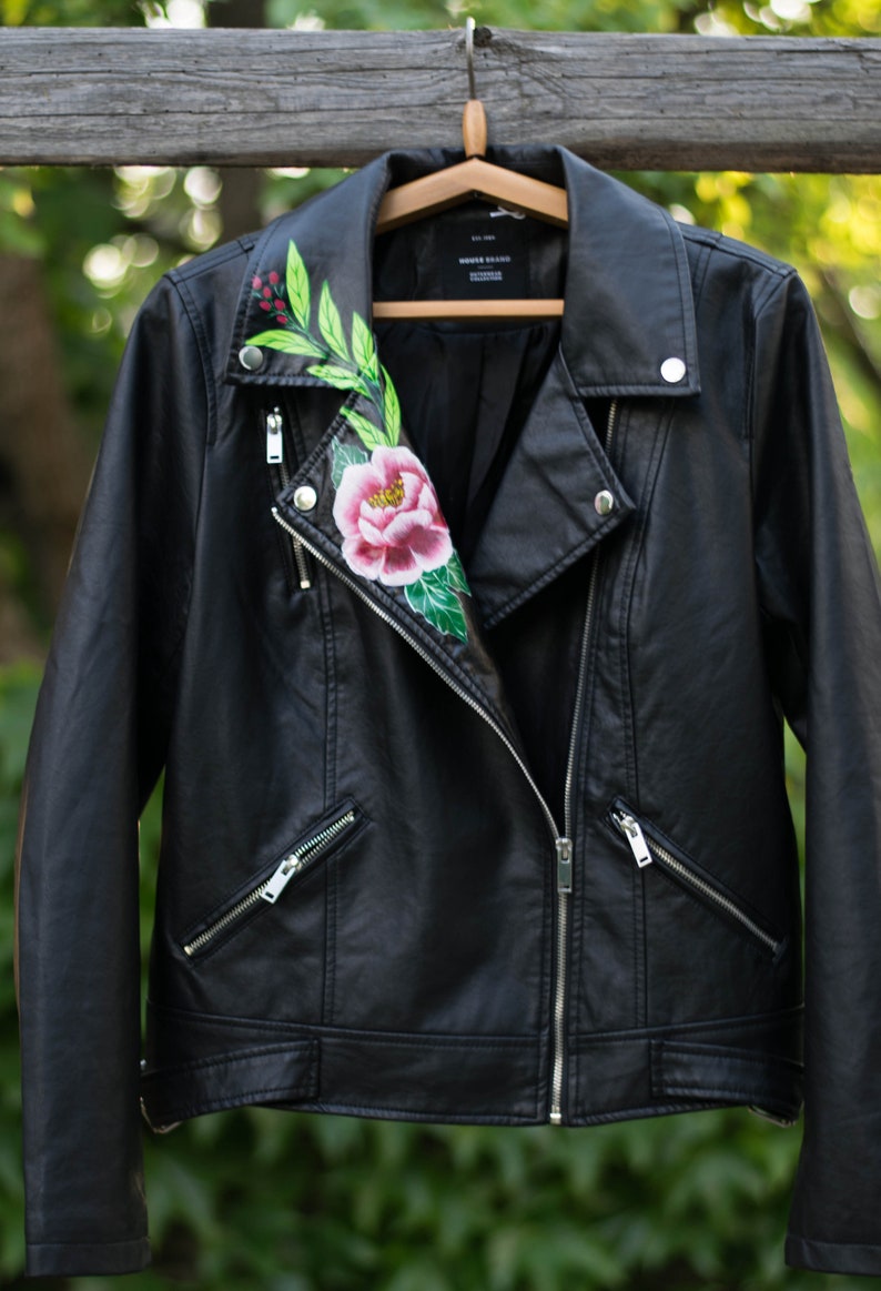 Puede incluir: Chaqueta de cuero negra para moto con un dise&ntilde;o floral pintado en el cuello. El dise&ntilde;o presenta una flor rosa, hojas verdes y bayas rojas.