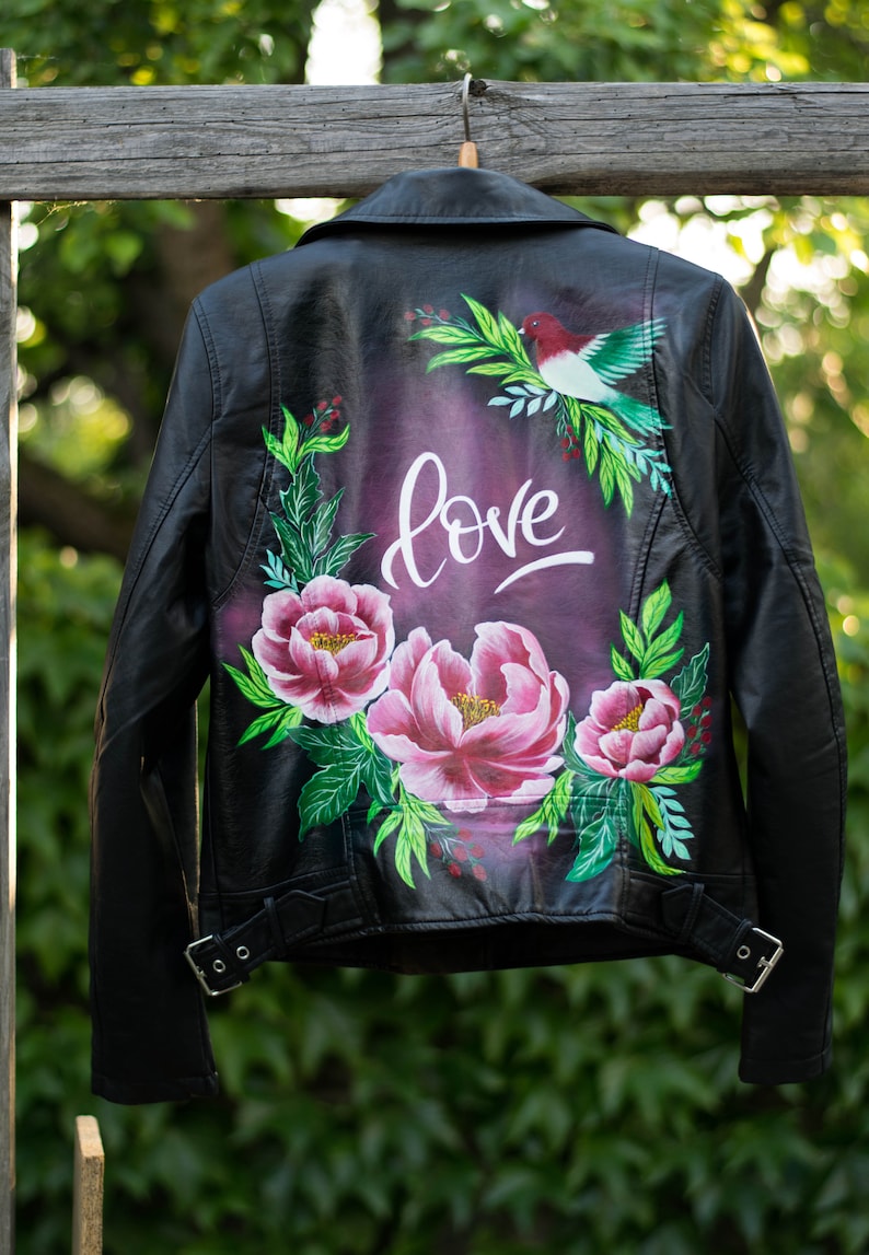 Puede incluir: Chaqueta de cuero negra con un dise&ntilde;o floral pintado en la espalda. El dise&ntilde;o incluye flores rosas, hojas verdes y la palabra "love" en letras blancas.