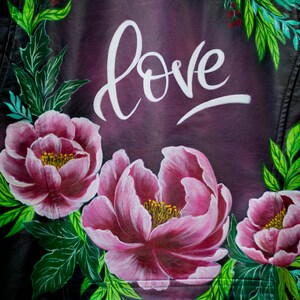 Puede incluir: Una chaqueta de cuero negra con un dise&ntilde;o pintado a mano con flores rosas, hojas verdes y la palabra "love" en escritura blanca.