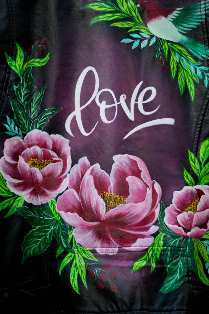 Puede incluir: Una chaqueta de cuero negra con un dise&ntilde;o pintado a mano con flores rosas, hojas verdes y la palabra "love" en escritura blanca.