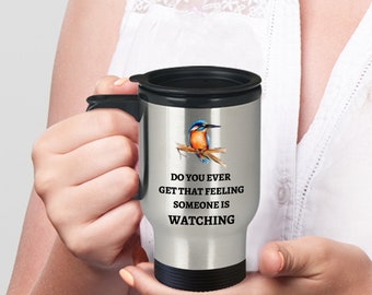 May include: A stainless steel travel mug with a black lid and handle. The mug features a colorful kingfisher bird perched on a branch and the text "Do you ever get that feeling someone is watching".