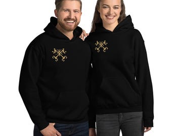 May include: Two people wearing black hooded sweatshirts. Each sweatshirt has a gold-colored emblem on the chest. The sweatshirts have a front pocket and a drawstring hood. The people are smiling.