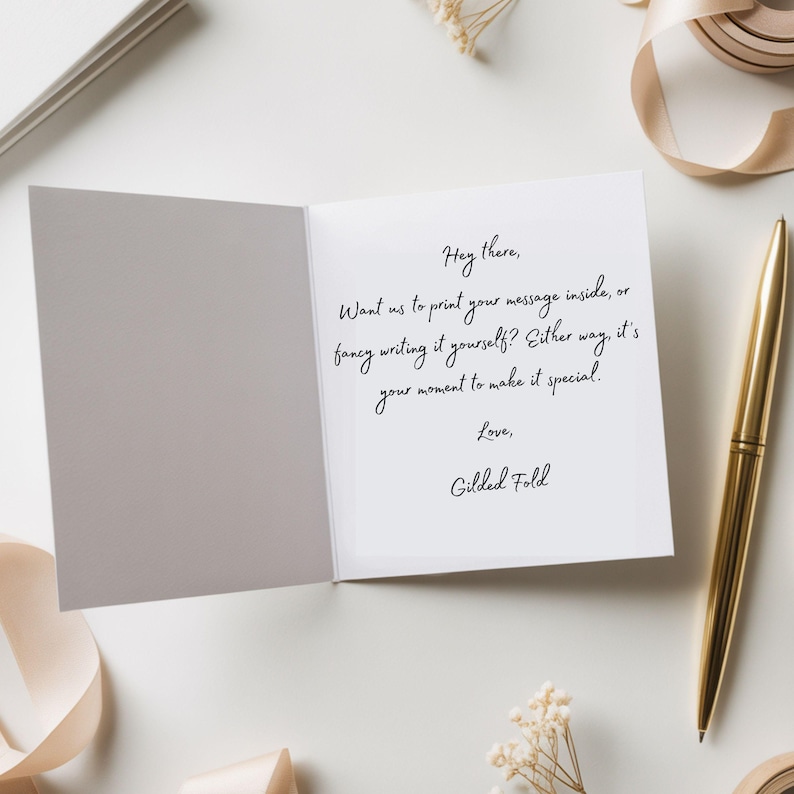 a white card with a handwritten message, a pen, and some decorative elements such as a ribbon and flowers.