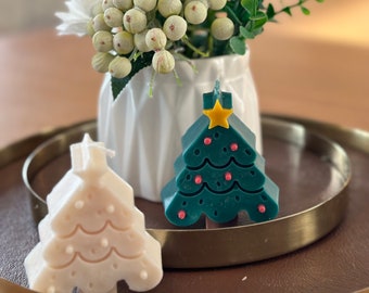May include: Two Christmas tree shaped candles, one is white and the other is green with red and yellow accents. The candles are on a gold tray.