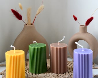 May include: Four pillar candles in different colors, yellow, green, brown, and purple. The candles are ribbed and have a natural, rustic look.