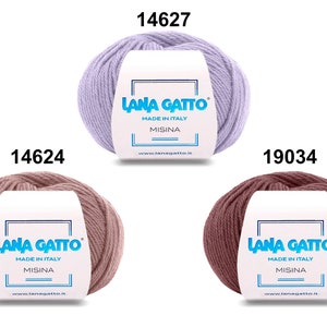 Op de afbeelding: Drie bollen garen in verschillende kleuren: lavendel, lichtroze en bruin. Elke bol heeft een wit etiket met de tekst "LANA GATTO" en "MADE IN ITALY" in blauwe tekst. Het etiket bevat ook de tekst "MISINA" in blauwe tekst. De bollen zijn ge&euml;tiketteerd met de nummers 14627, 14624 en 19034.