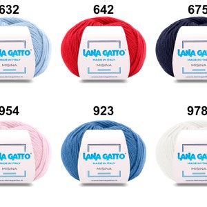 Op de afbeelding: Zes bollen garen in verschillende kleuren: lichtblauw, rood, donkerblauw, roze, blauw en wit. Elke bol heeft een label met de tekst "Lana Gatto" en "Made in Italy" met het nummer van de kleur bovenaan.
