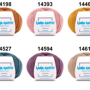 Op de afbeelding: Zes bollen Lana Gatto Misina garen in verschillende kleuren, waaronder oranje, roze, geel, blauw, paars en beige. Elke bol heeft een label met de merknaam en "Made in Italy".