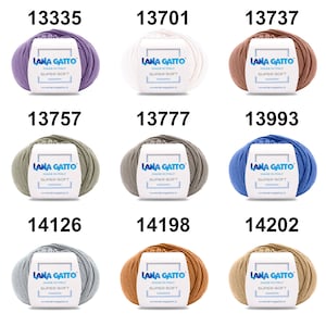 May include: Nine balls of yarn in various colors, including purple, white, brown, green, gray, blue, light gray, orange, and beige. Each ball has a label that reads "Lana Gatto Made in Italy Super Soft" and a website address.