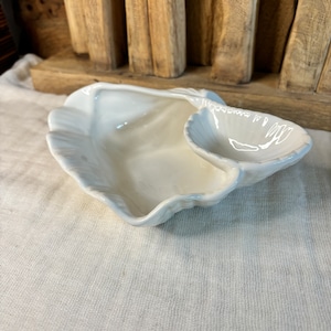 May include: White ceramic seashell dish with two sections. The larger section is a shallow bowl and the smaller section is a deep bowl.