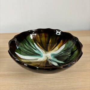 May include: A small, round ceramic bowl with a wavy rim. The bowl is decorated with a swirling pattern of brown, green, and white glaze.