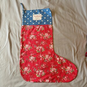 May include: A festive Christmas stocking featuring a red floral design and a blue polka dot top. It has a hanging loop and a label that reads "Merry Christmas".
