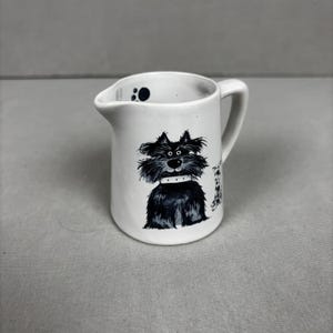 May include: A set of three ceramic mugs with a speckled, matte finish. The mugs are in shades of cream, light gray, and dark gray. Each mug has a simple, minimalist design and a rounded handle.