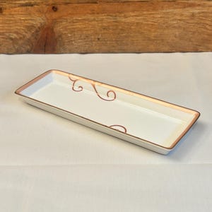 May include: A white rectangular serving tray with a thin, gold-coloured rim and a delicate, swirling design in gold.